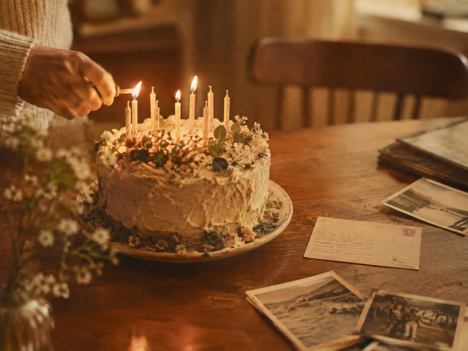 A birthday cake with lit candles beside a handwritten postcard and old photographs